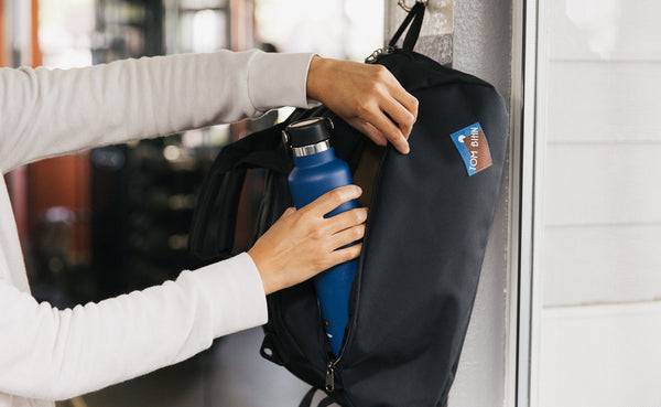 OSCA hanging on the hook at a gym; a person is removing a water bottle from one of the side 3D pockets.